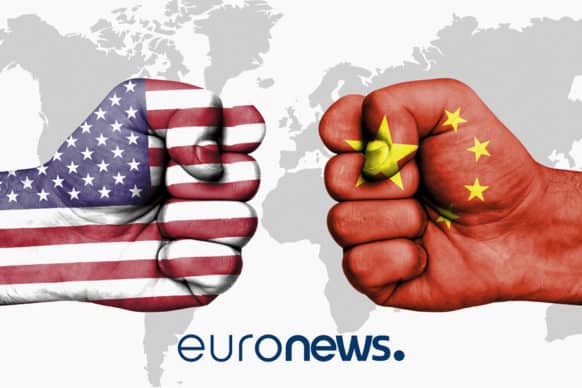 Deux poings se font face, l'un portant le drapeau américain et l'autre le drapeau chinois, symbolisant la rivalité économique. En arrière-plan, une carte du monde grisée. Logo 'euronews' en bas de l'image. Stratégies avancées de gestion du risque de change 2025.