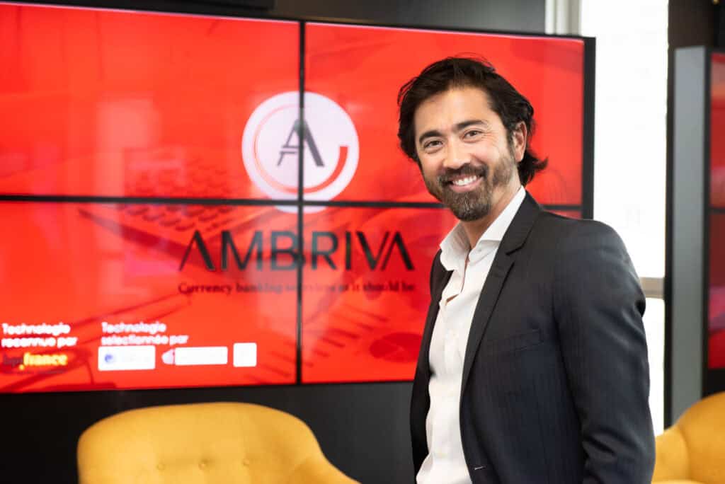 Sébastien Oum fondateur d’Ambriva devant le logo de l’entreprise spécialisée en gestion du risque de change